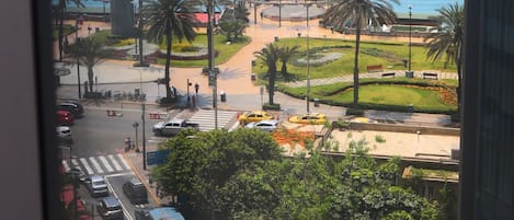 Vista de una zona costera con un edificio moderno, una estructura circular y un parque con palmeras.