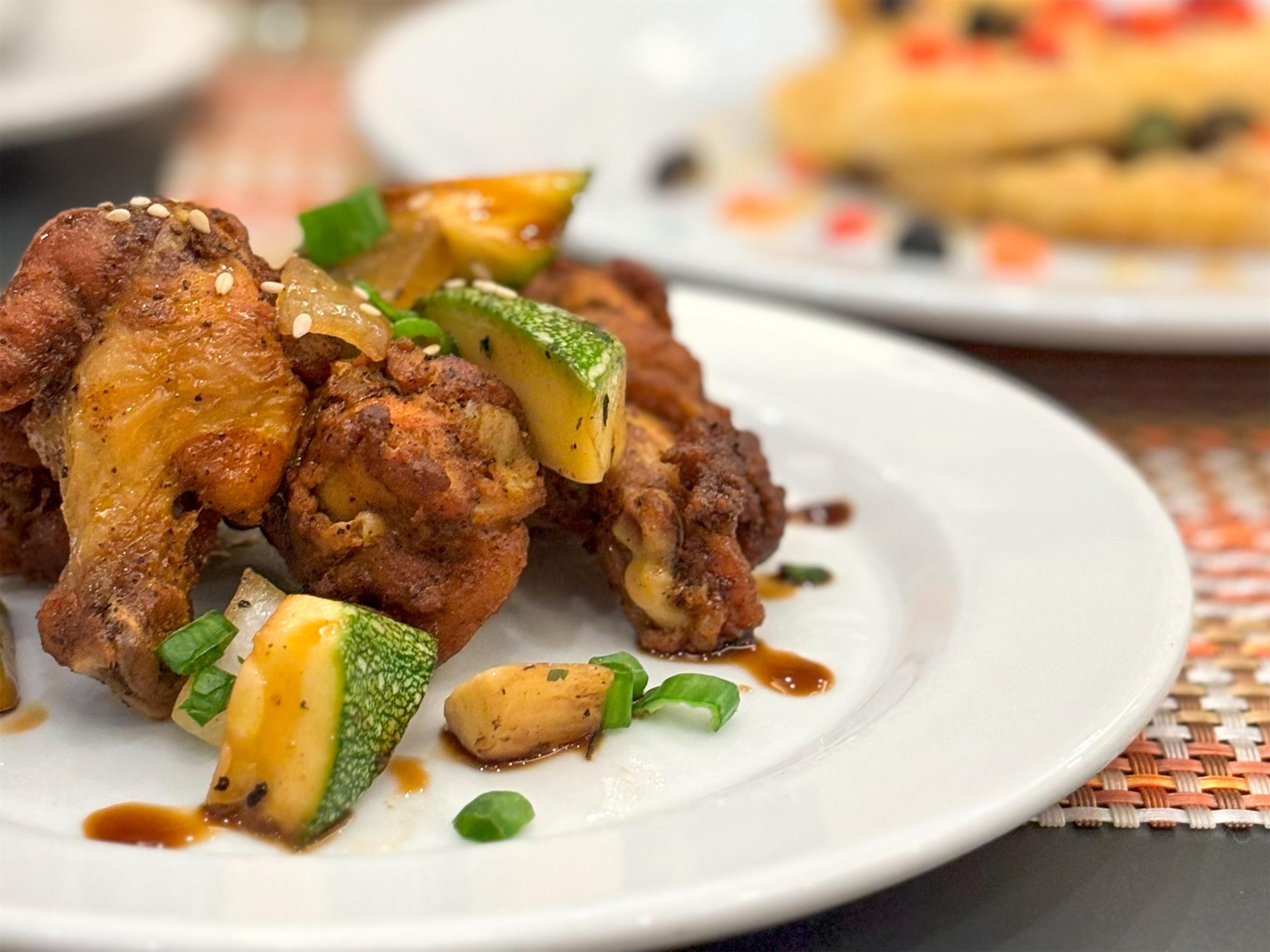 Un plato de pollo frito con semillas de sésamo y cebollines, sobre un plato blanco.