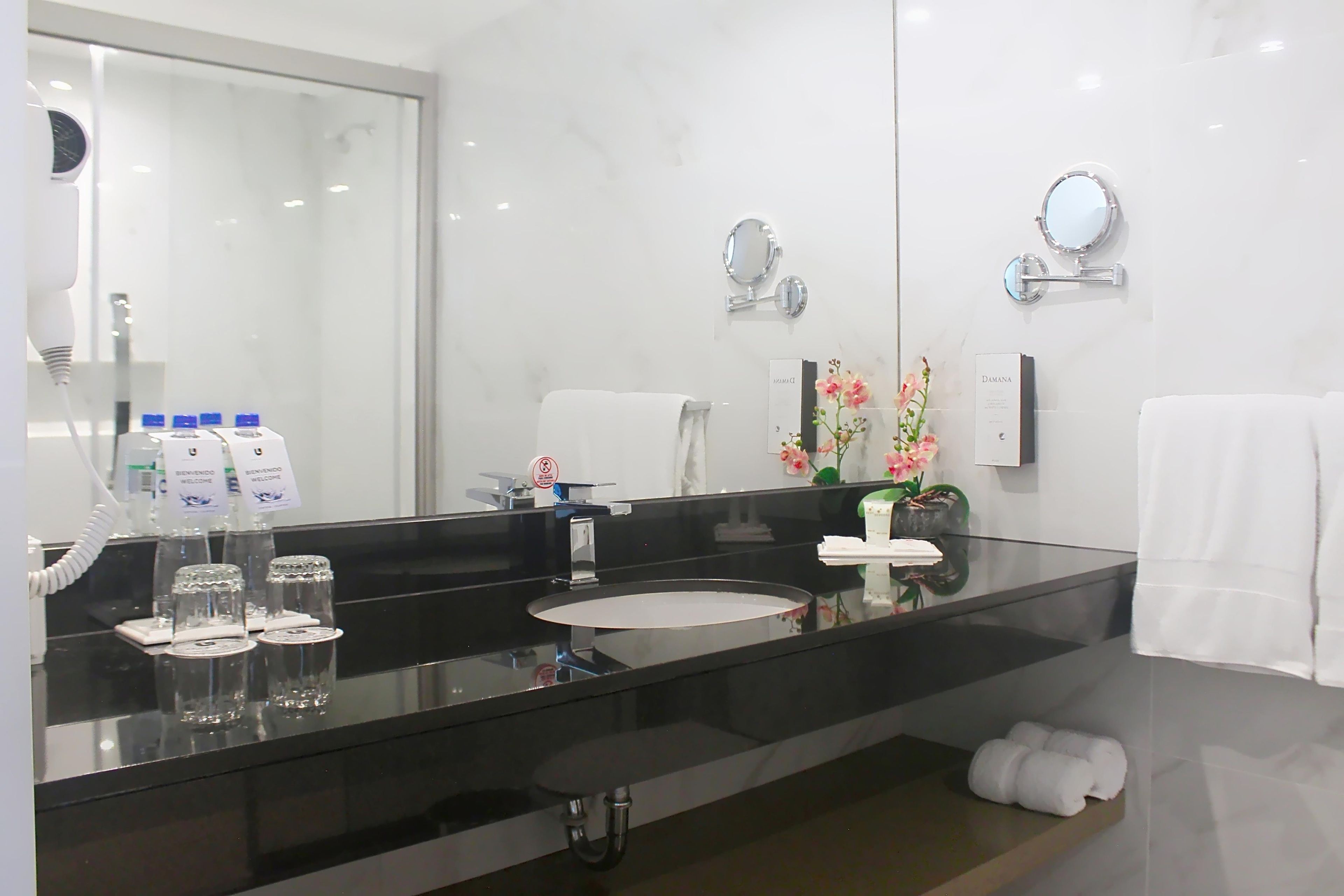 A modern bathroom with a black countertop, a sink, a large mirror, and a towel rack.