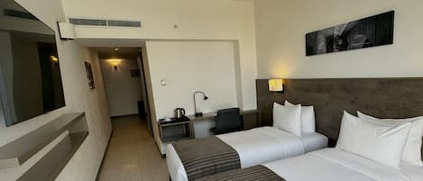 Habitación de hotel con dos camas, un escritorio con silla, un televisor y un cuadro en la pared.