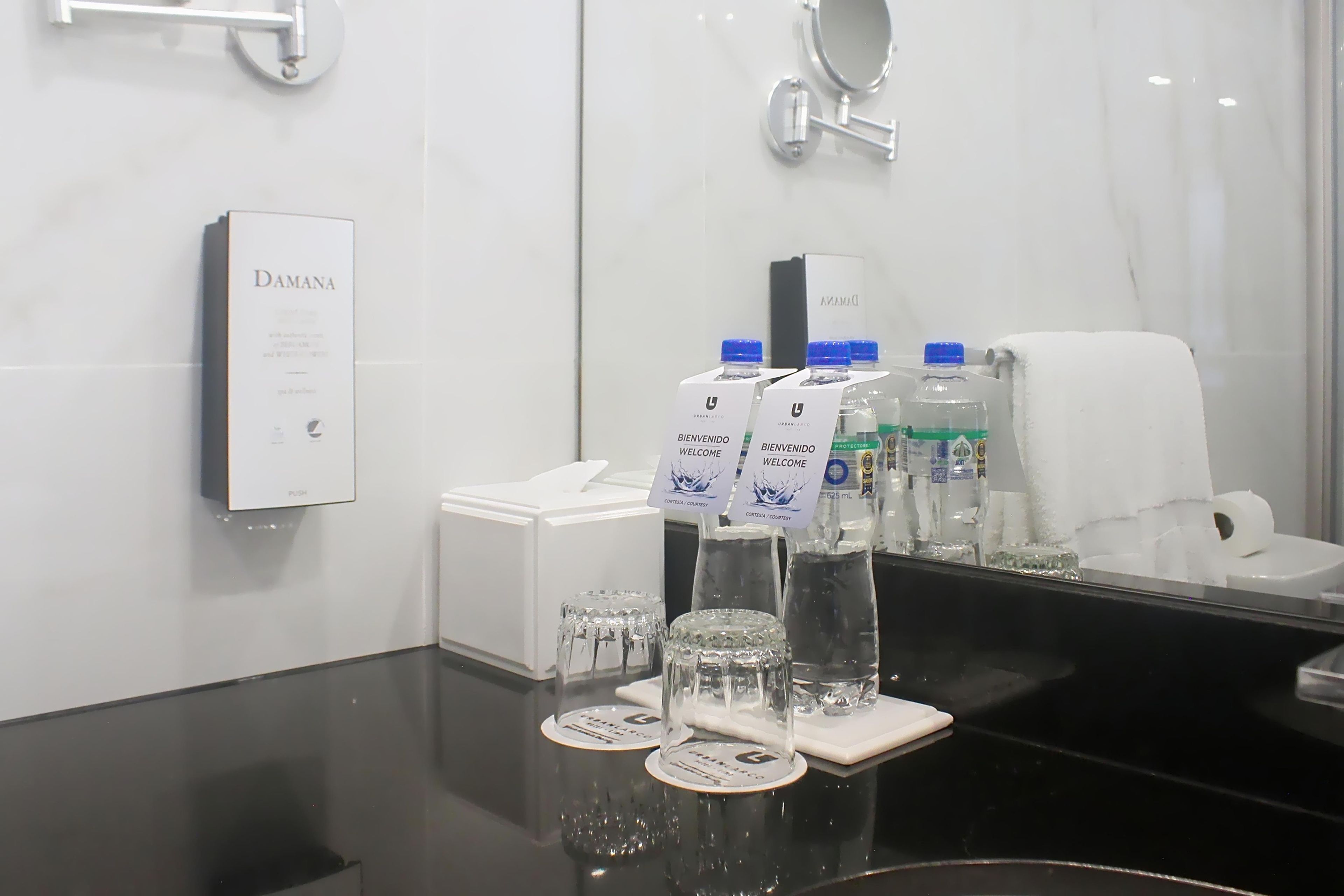 Baño de hotel con espejo, dispensador de gel antibacterial y caja de pañuelos.