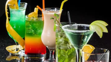 Forskellige farverige cocktails med sugerør og pynt, vist på en reflekterende overflade mod en mørk baggrund.