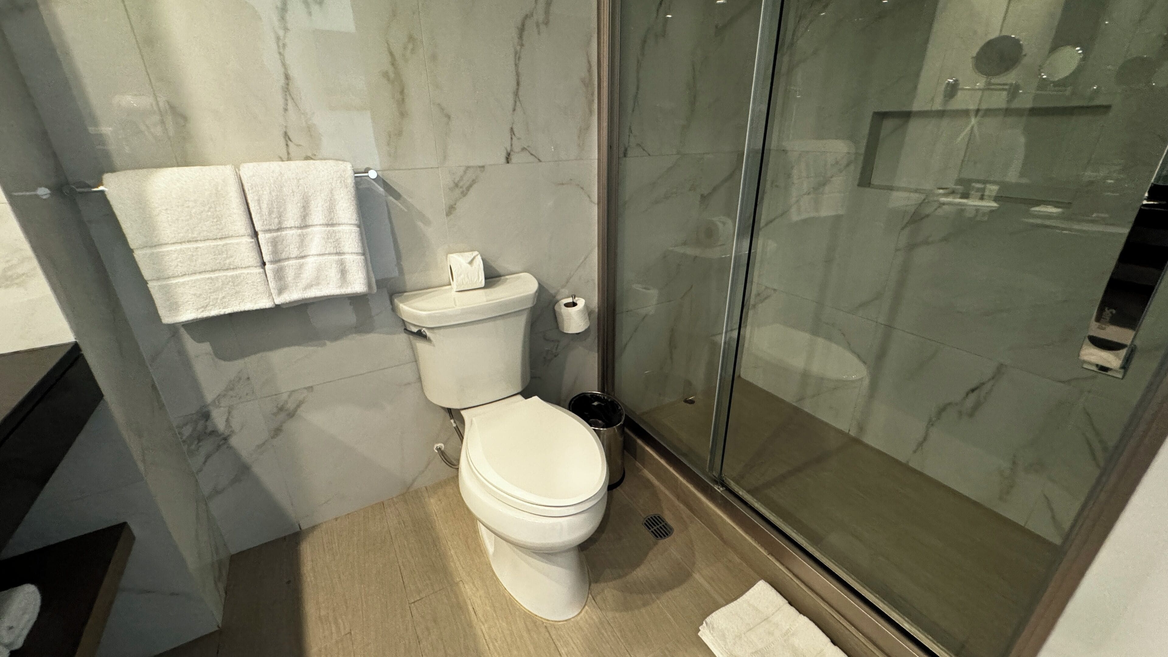 A modern bathroom with a toilet, a glass shower enclosure, and marble walls.