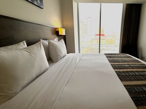 A hotel room with a large bed, a headboard, a nightstand with a lamp, and a view of buildings through the window. - Best Western Plus Urban Larco Hotel (Lima)