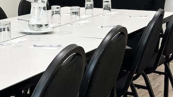 A conference room with a long table, black chairs, and a coffee station with two coffee makers.