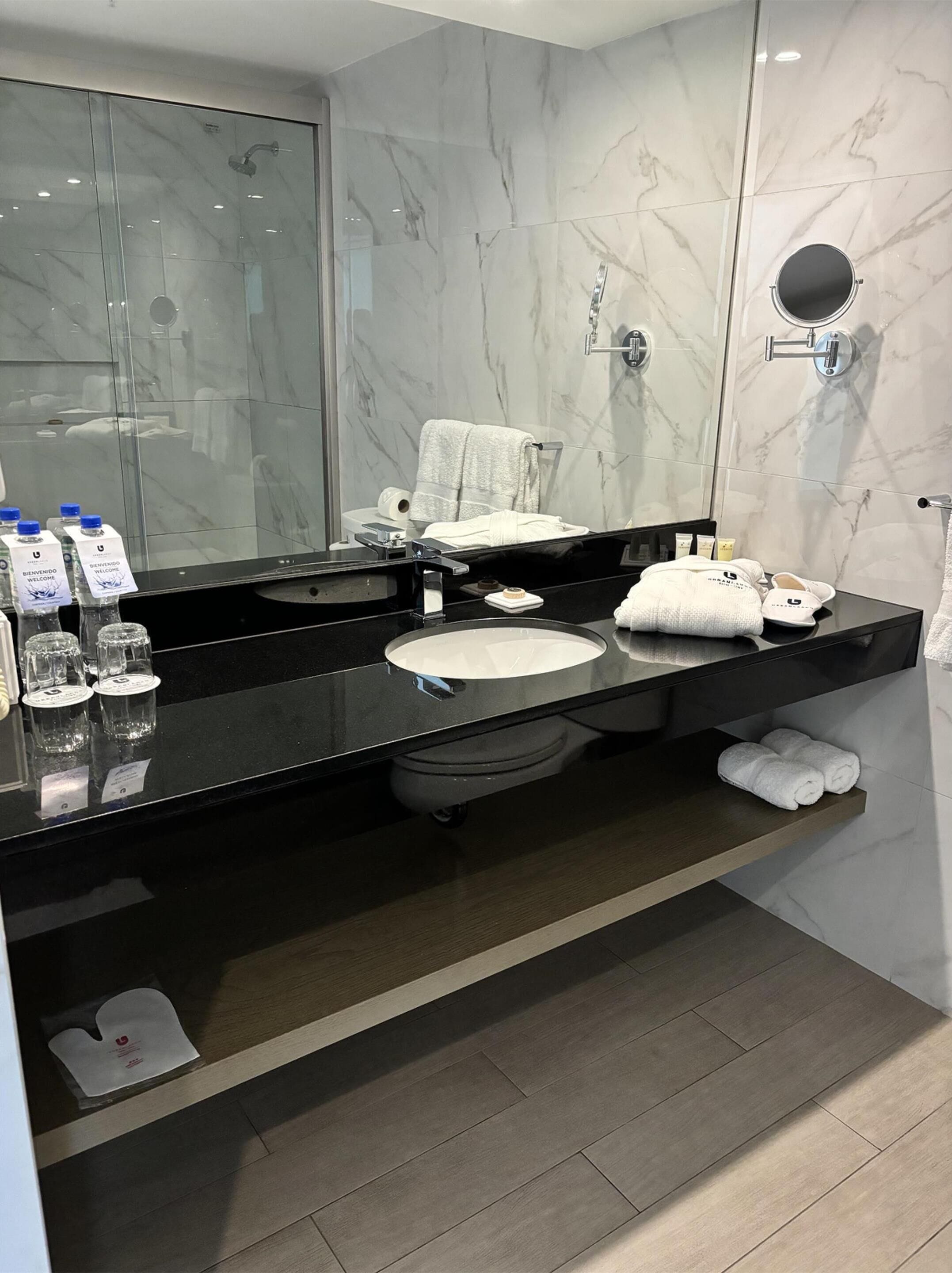 Un baño moderno con encimera negra, un lavabo redondo y cabina de ducha con mampara de vidrio.