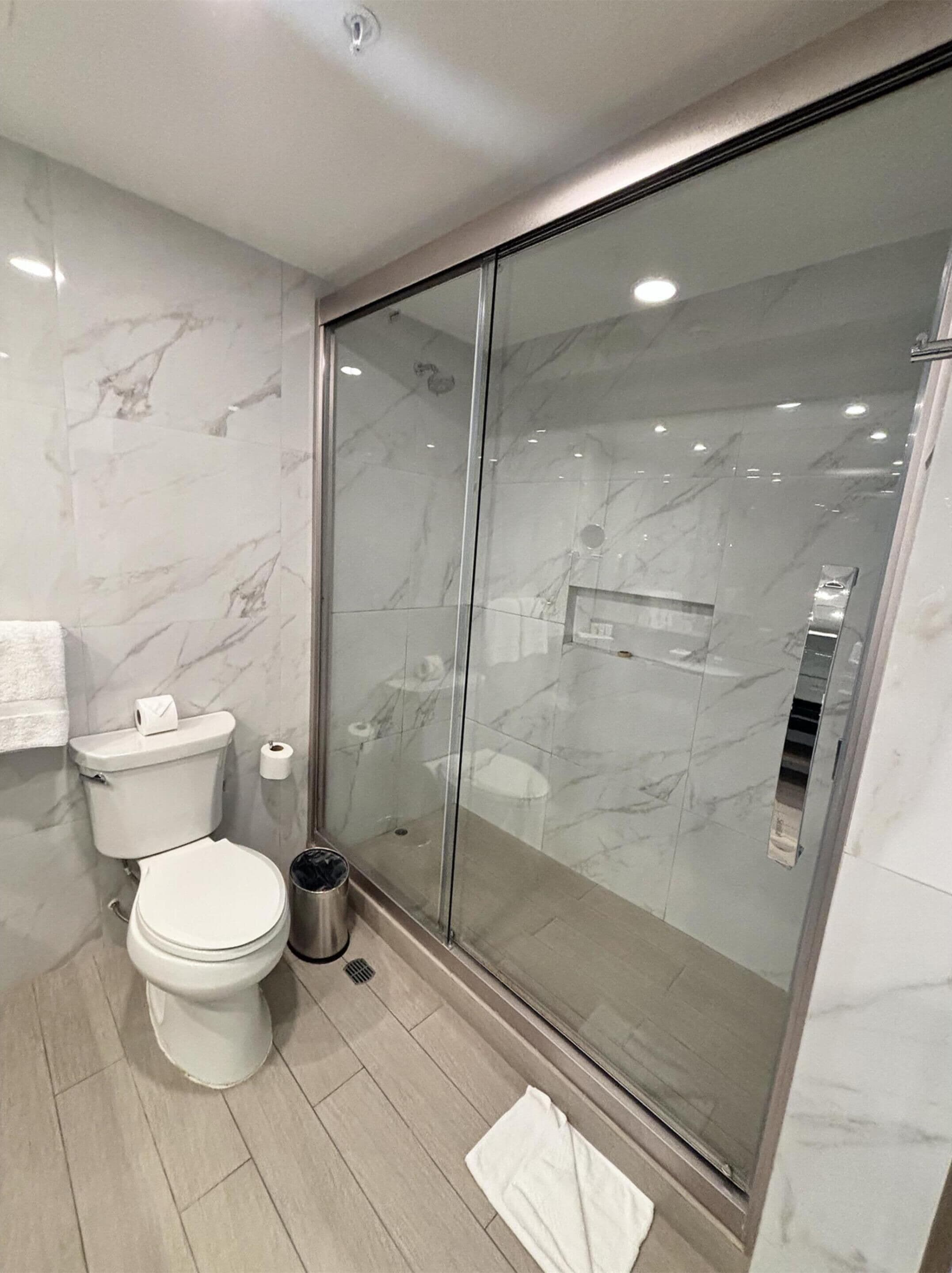 Un baño moderno con cabina de ducha de vidrio, inodoro y un cubo de basura.