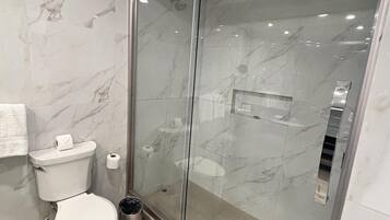 Un baño moderno con cabina de ducha de vidrio, inodoro y un cubo de basura.