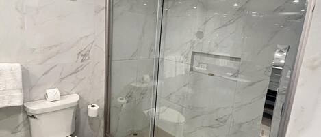 A modern bathroom with a glass shower enclosure, a toilet, and a trash bin.