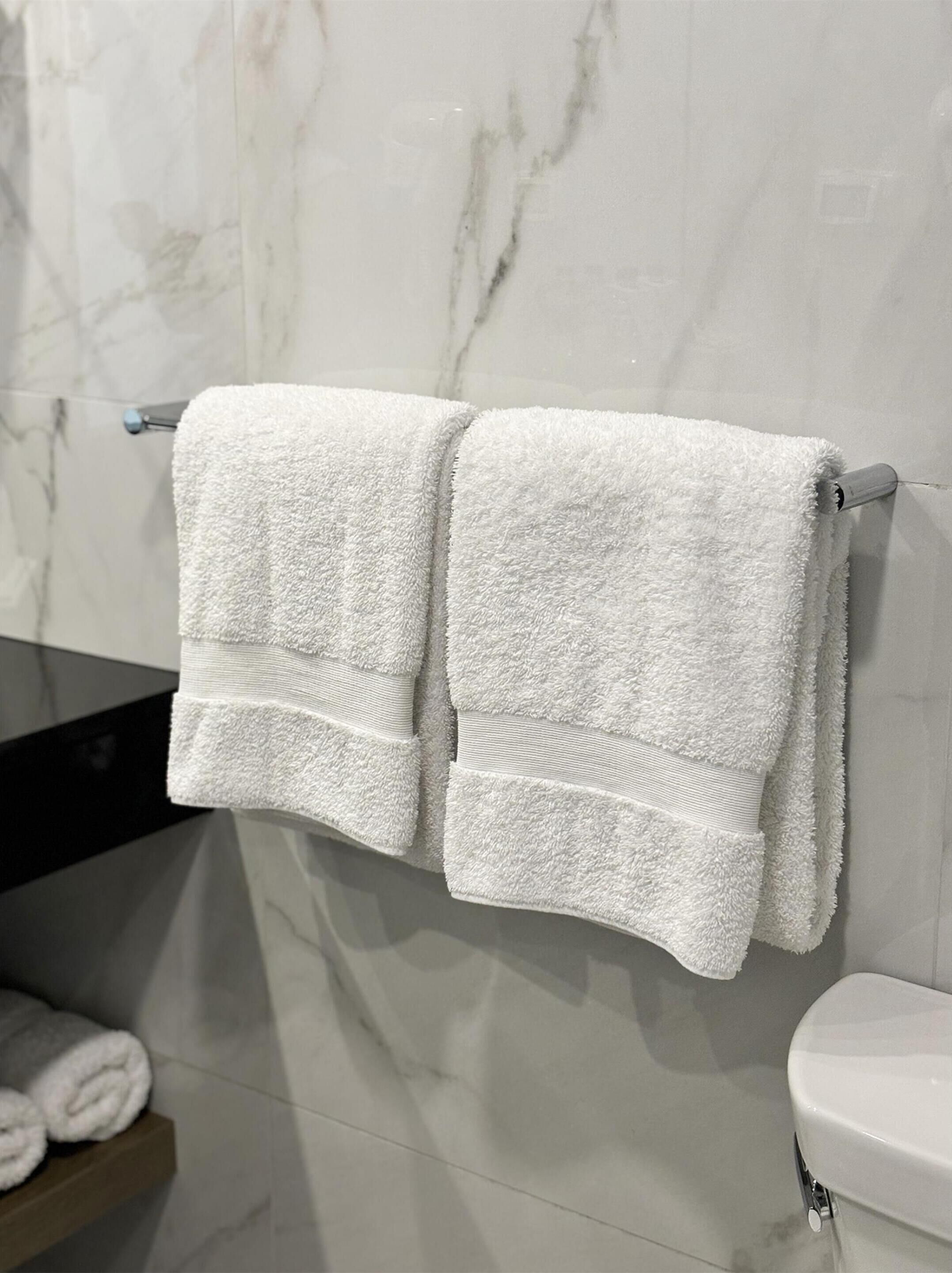 A bathroom with two white towels hanging on a towel rack, a marble wall, and a toilet.