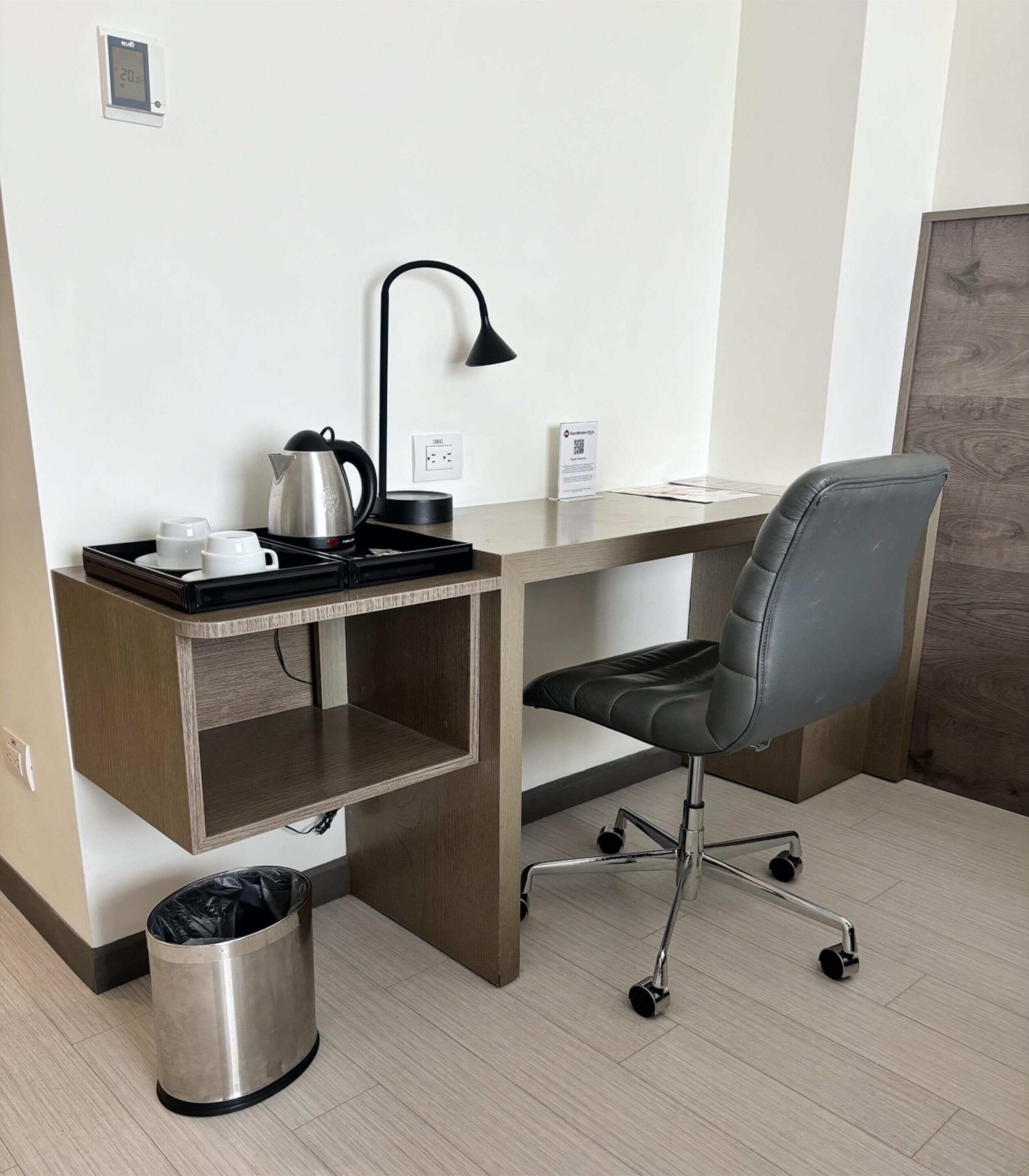 Un petit espace de bureau comprenant un bureau, une chaise, une bouilloire et une poubelle.
