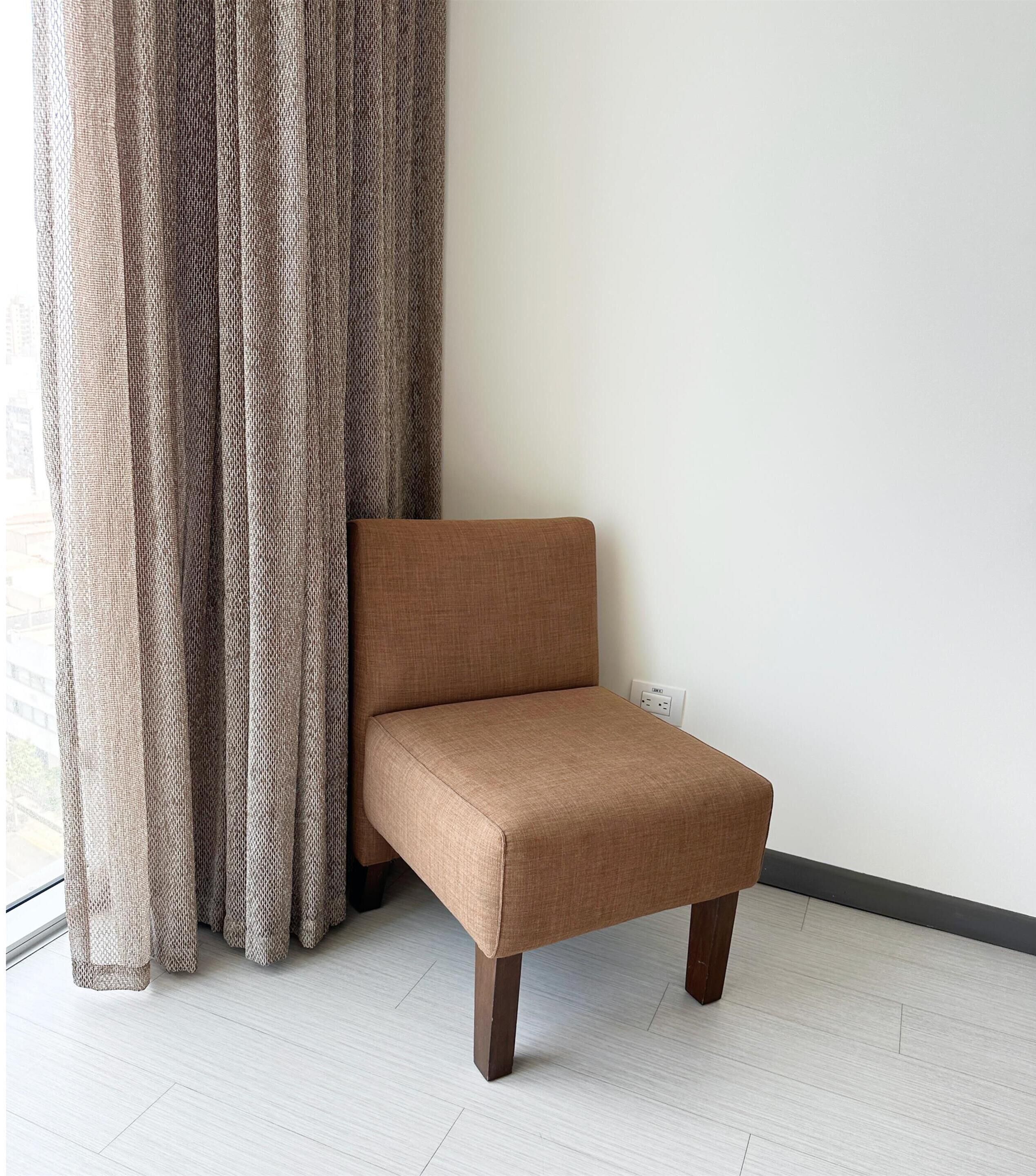 Un fauteuil marron, avec des pieds en bois, est placé contre un mur blanc, à proximité d’une prise de courant.