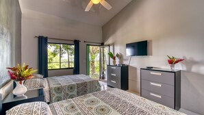 A hotel room with two beds, a ceiling fan, a TV, a dresser, and a window with curtains. - Casa Conley del Mar (Cahuita)