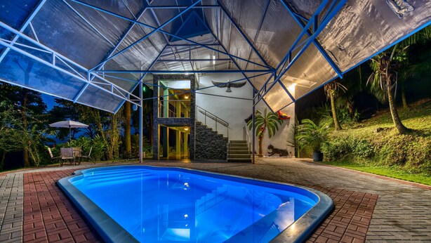 A swimming pool with a geometric roof structure, surrounded by a brick pathway and tropical plants. - Casa Conley del Mar (Cahuita)