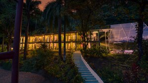 A modern building with a glass facade, surrounded by lush greenery and a pathway leading to the entrance. - Casa Conley del Mar (Cahuita)