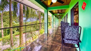 A corridor with ceiling fans, chairs, and a view of tropical trees. - Casa Conley del Mar (Cahuita)