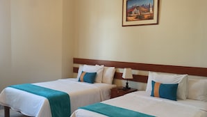 Quarto de hotel com duas camas, uma mesinha de cabeceira, uma luminária e um quadro na parede.