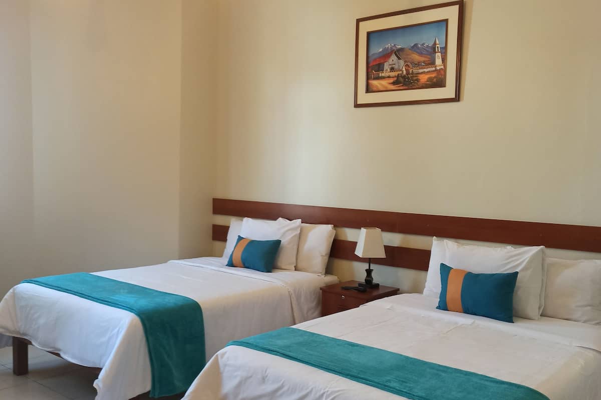 Habitación de hotel con dos camas, una mesita de noche, una lámpara y un cuadro en la pared.