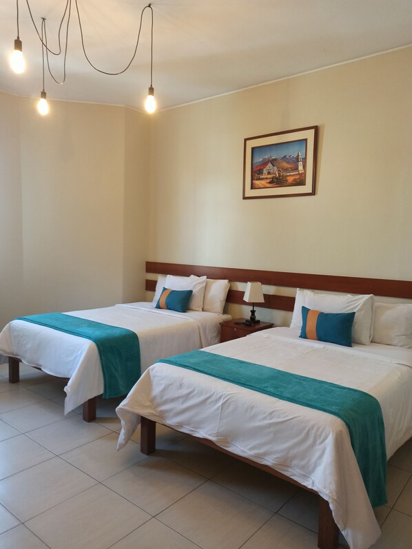 A hotel room with two beds, a nightstand, a lamp, and a painting on the wall. - Nasara (Arequipa)
