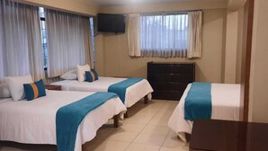 Quarto de hotel com três camas, televisão na parede, mesa de madeira e janela com cortinas.