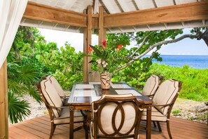 A wooden deck with a table and chairs, surrounded by lush greenery and overlooking the ocean. - Sea Lodge 2 People (Roatan)
