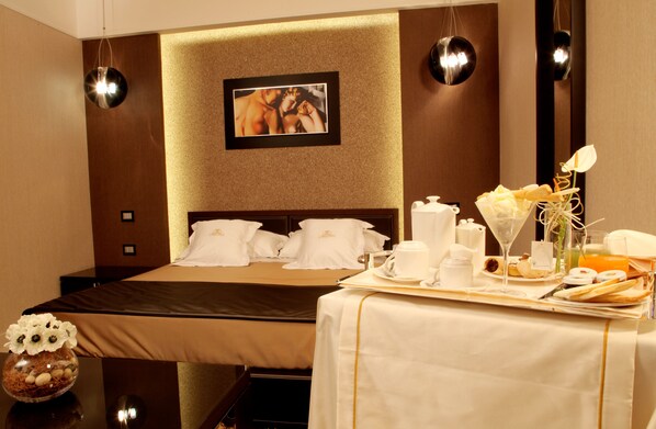 A hotel room with a neatly made bed, a breakfast tray with pastries and coffee, and a vase with flowers on the side table.