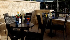 Un patio al aire libre con muros de piedra, sillas de mimbre y mesas listas para comer.