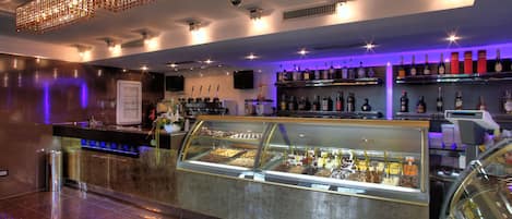 A modern bar area with a display case of desserts, a selection of liquor bottles, and a chandelier.