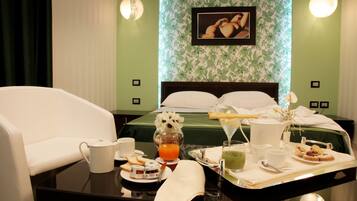 A neatly arranged hotel room with a bed, a white sofa, a breakfast tray with food and drinks, and a framed picture on the wall.