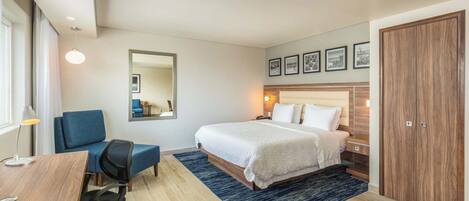 A hotel room with a bed, a desk, a chair, a mirror, and a wardrobe.