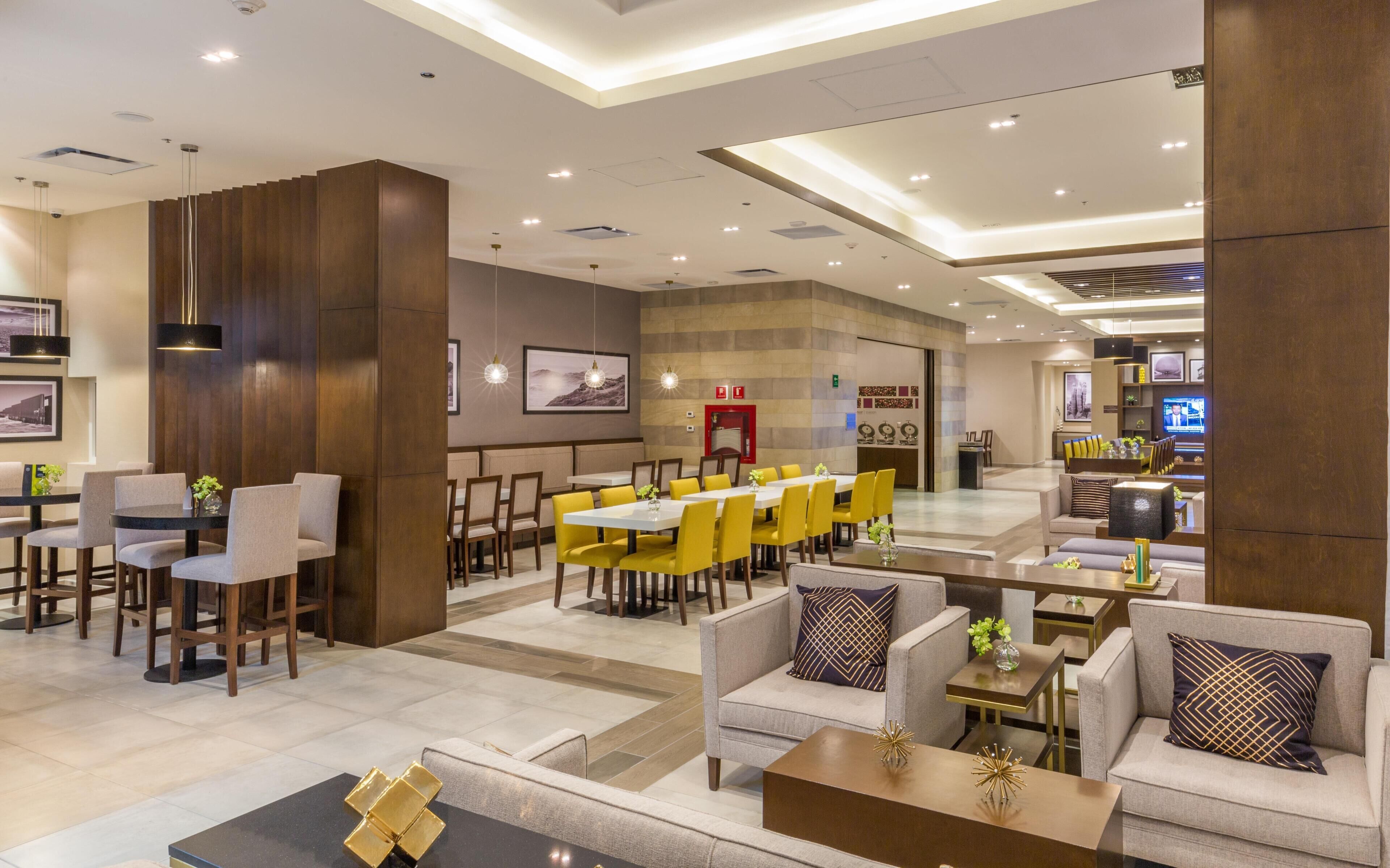 A hotel lobby with a dining area, sofas, and a TV.