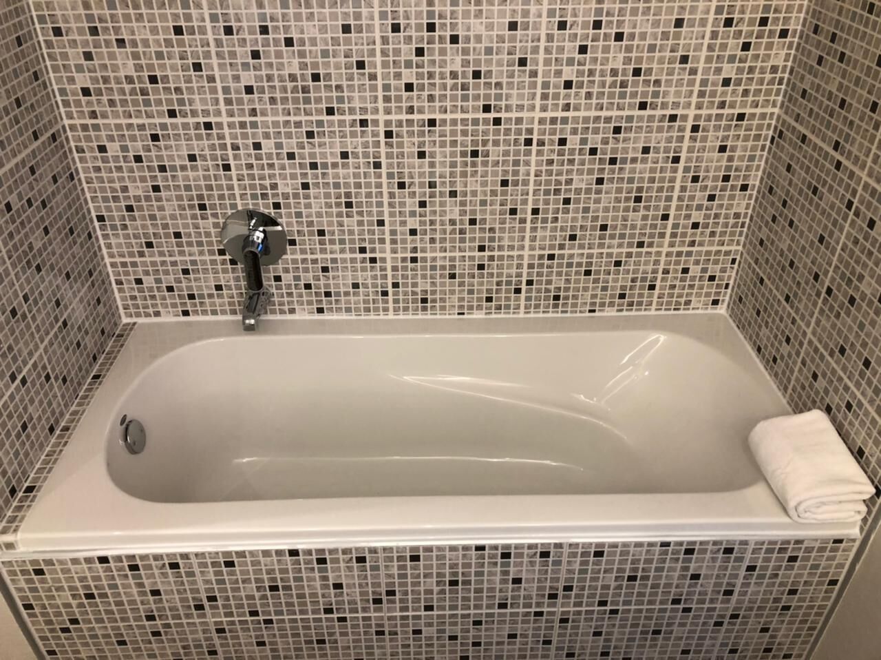 A rectangular bathtub with a faucet and a towel on the right side. The walls are tiled with a mosaic pattern.