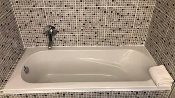 A rectangular bathtub with a faucet and a towel on the right side. The walls are tiled with a mosaic pattern.