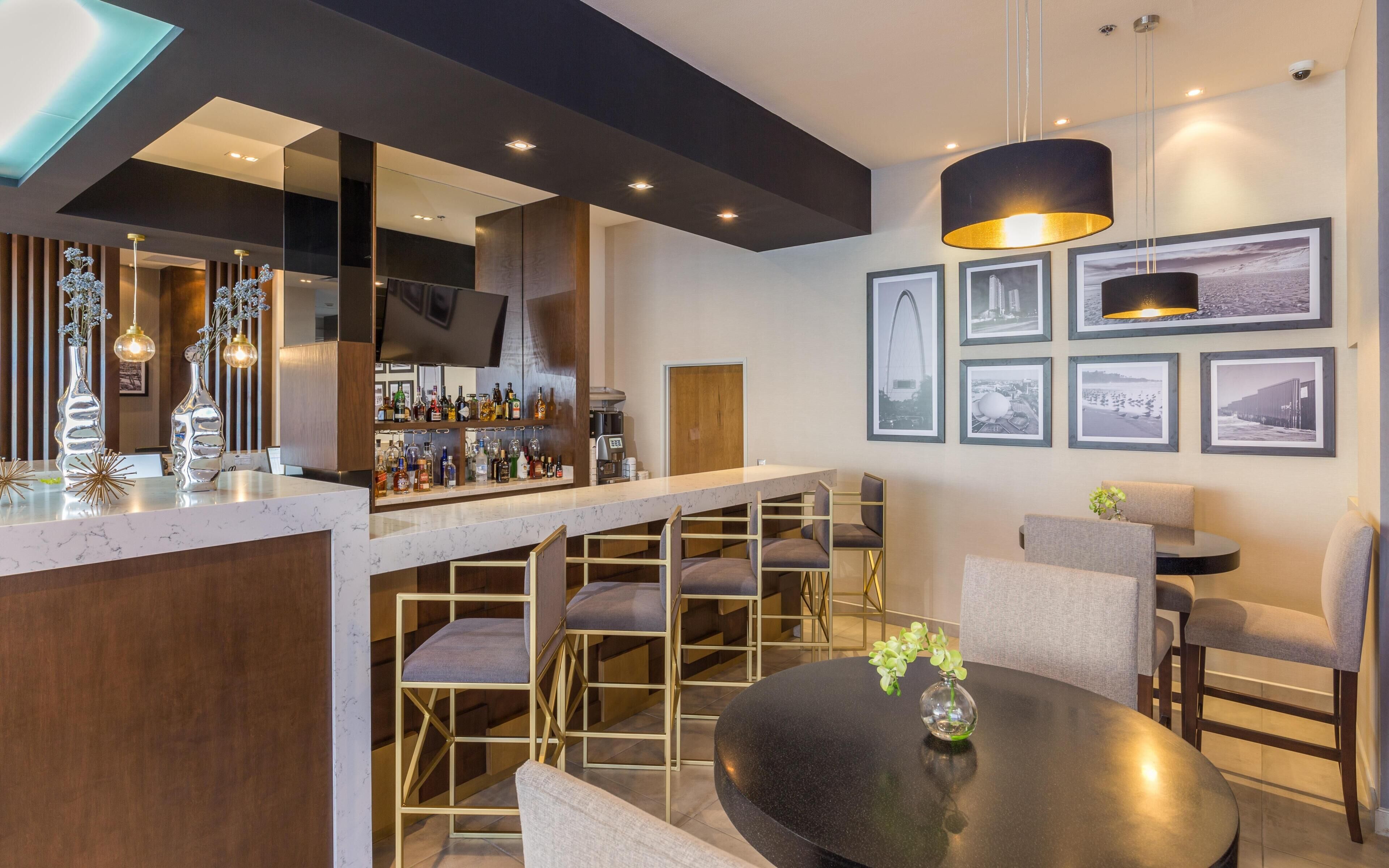 Zona de bar moderna con encimera de mármol, diversas opciones de asientos y una variedad de botellas de licor.