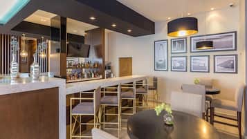 Zona de bar moderna con encimera de mármol, diversas opciones de asientos y una variedad de botellas de licor.