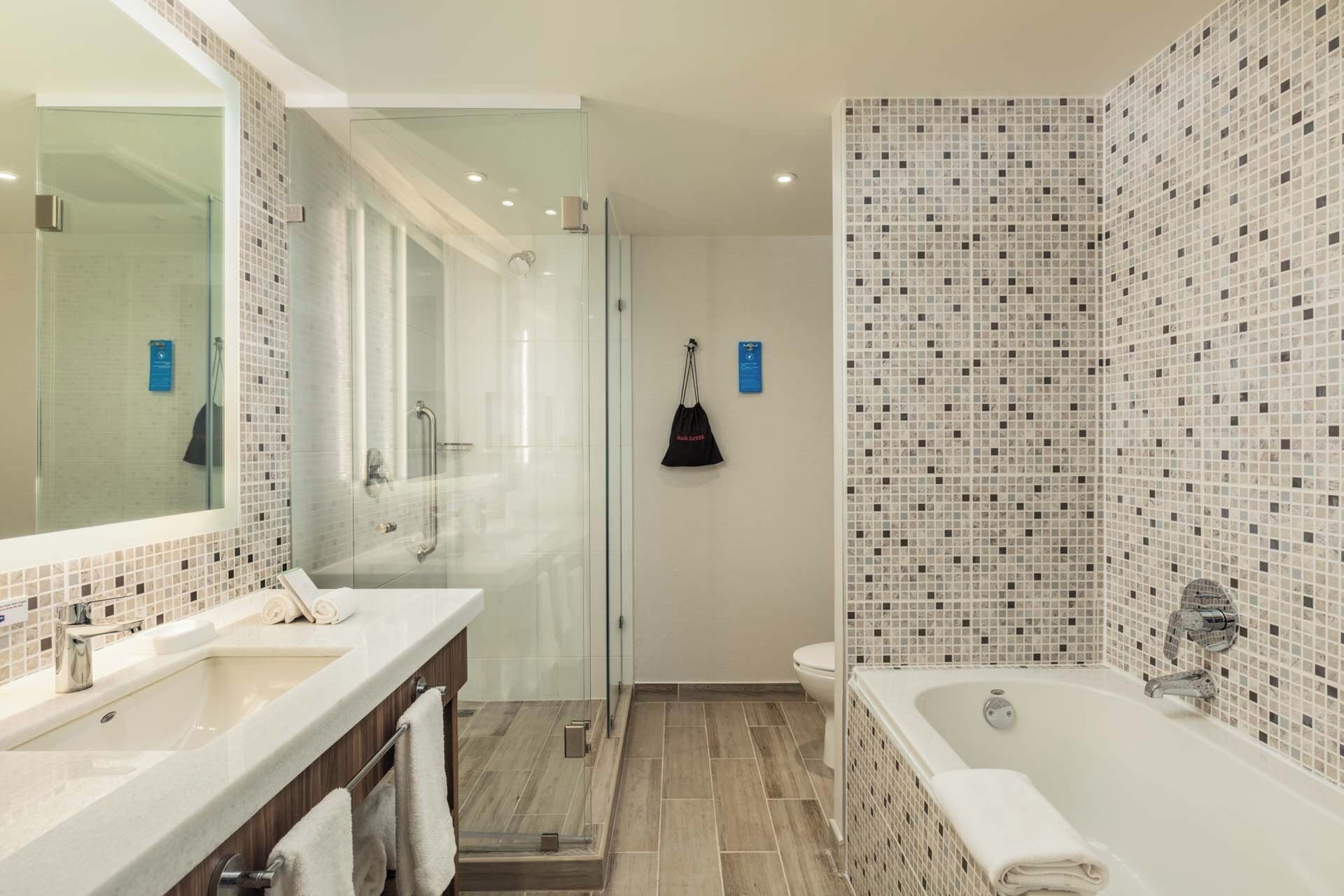 A modern bathroom with a glass shower enclosure, a large bathtub, and a vanity with a mirror.