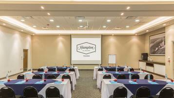 A conference room with multiple tables, chairs, a projector screen, and a presentation on the wall.
