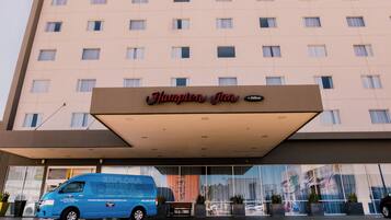 Un hotel Hampton Inn con una camioneta azul estacionada frente, ventanas amplias y un cielo despejado.