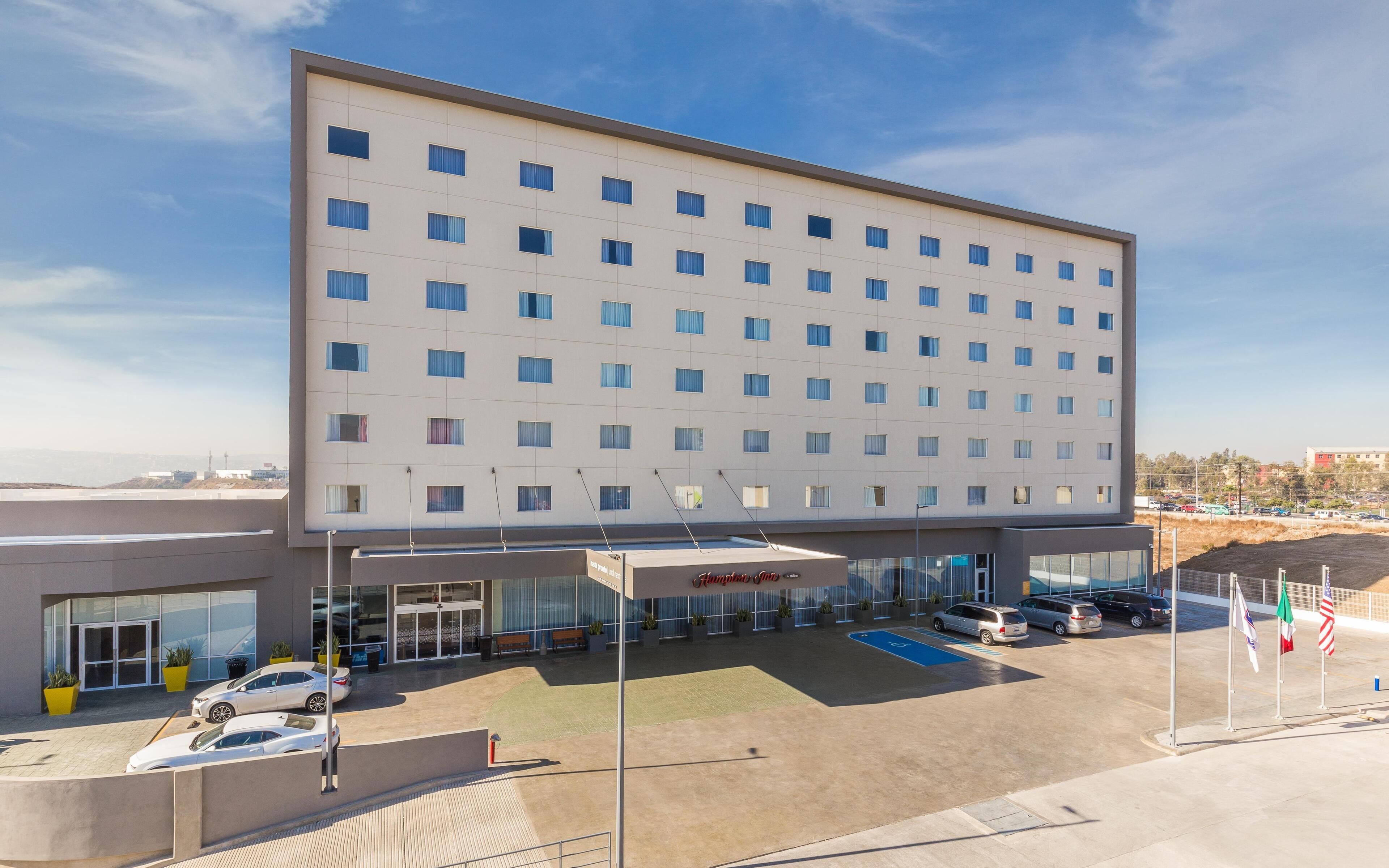 A modern hotel with a flat facade, multiple windows, and a parking lot with several cars.