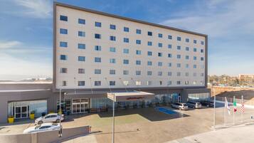 A modern hotel with a flat facade, multiple windows, and a parking lot with several cars.