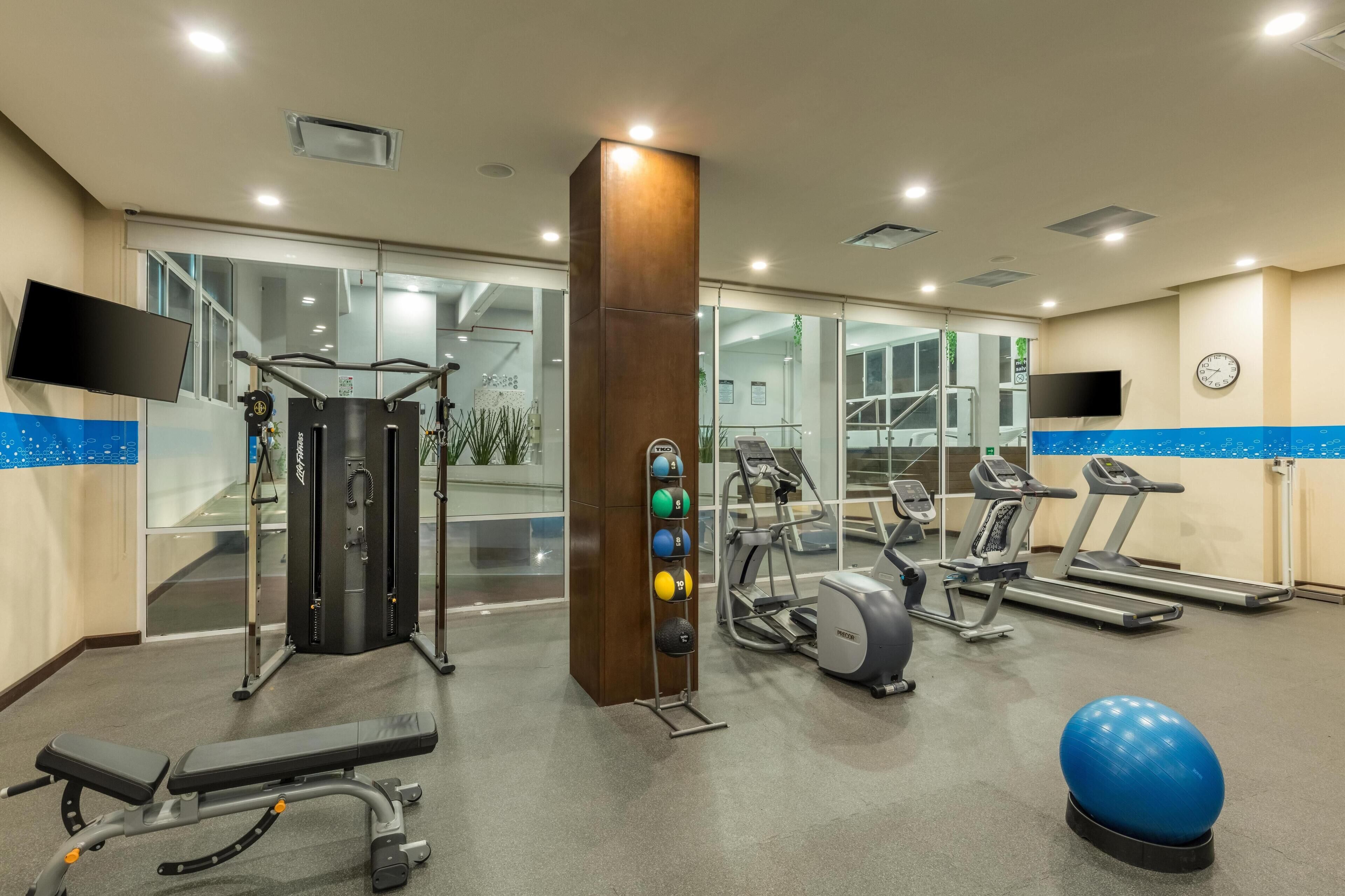 A gym with exercise equipment, a bench, a ball, and a clock on the wall.