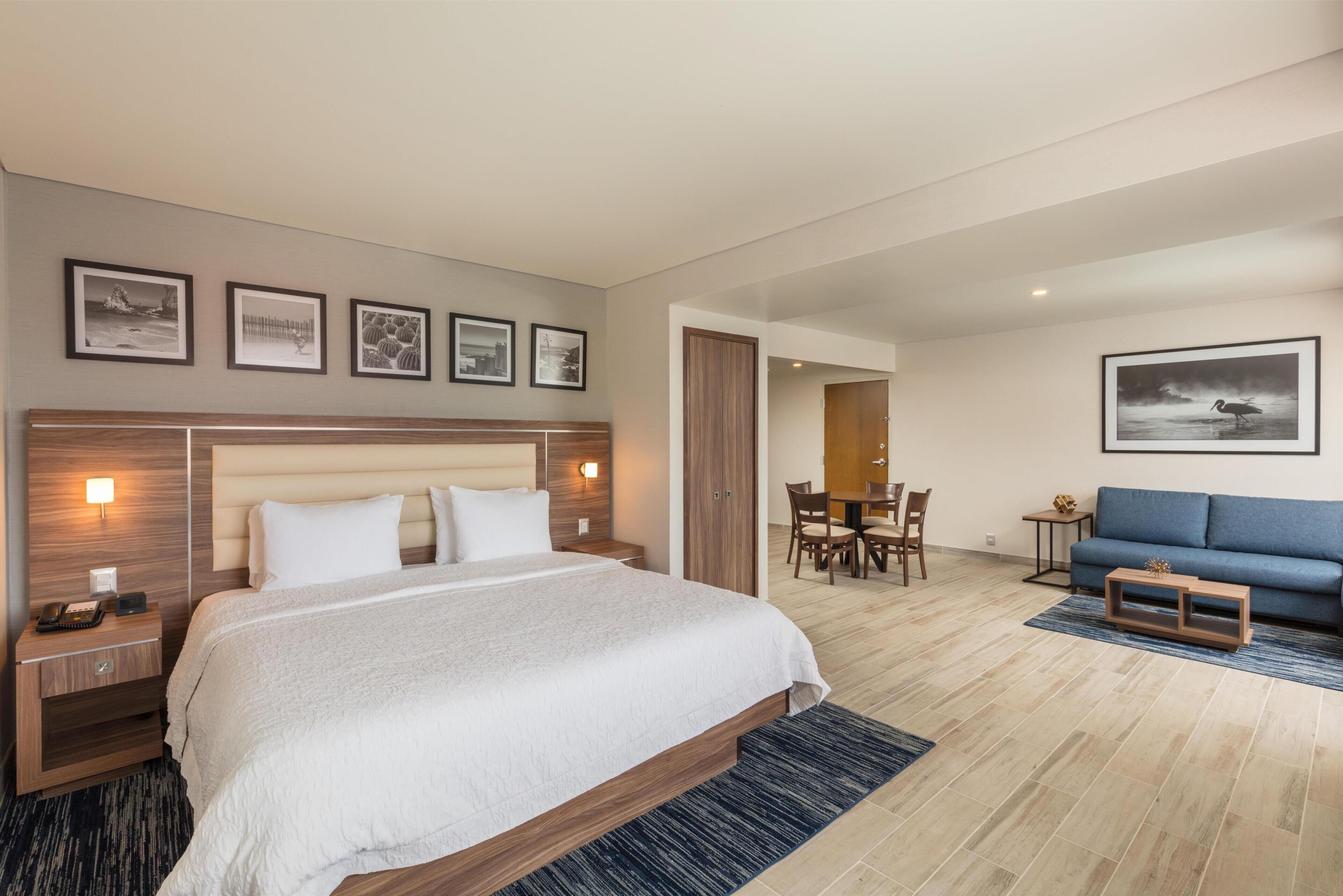 A hotel room with a large bed, a desk, a sofa, and a dining area.
