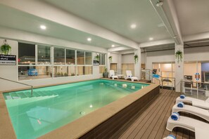 Piscina interna com cadeiras de lounge, placa indicando posto de salva-vidas e vista para o exterior.