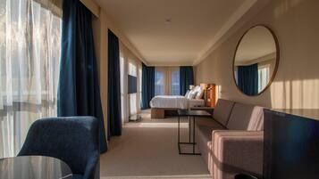 Een hotelkamer met een bed, een bank, een tafel, een spiegel en uitzicht op het omliggende landschap.