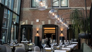 A restaurant with brick walls, large windows, and hanging spherical light fixtures. Tables are set with wine glasses and plates. - Pestana Amsterdam Riverside (Amsterdam)