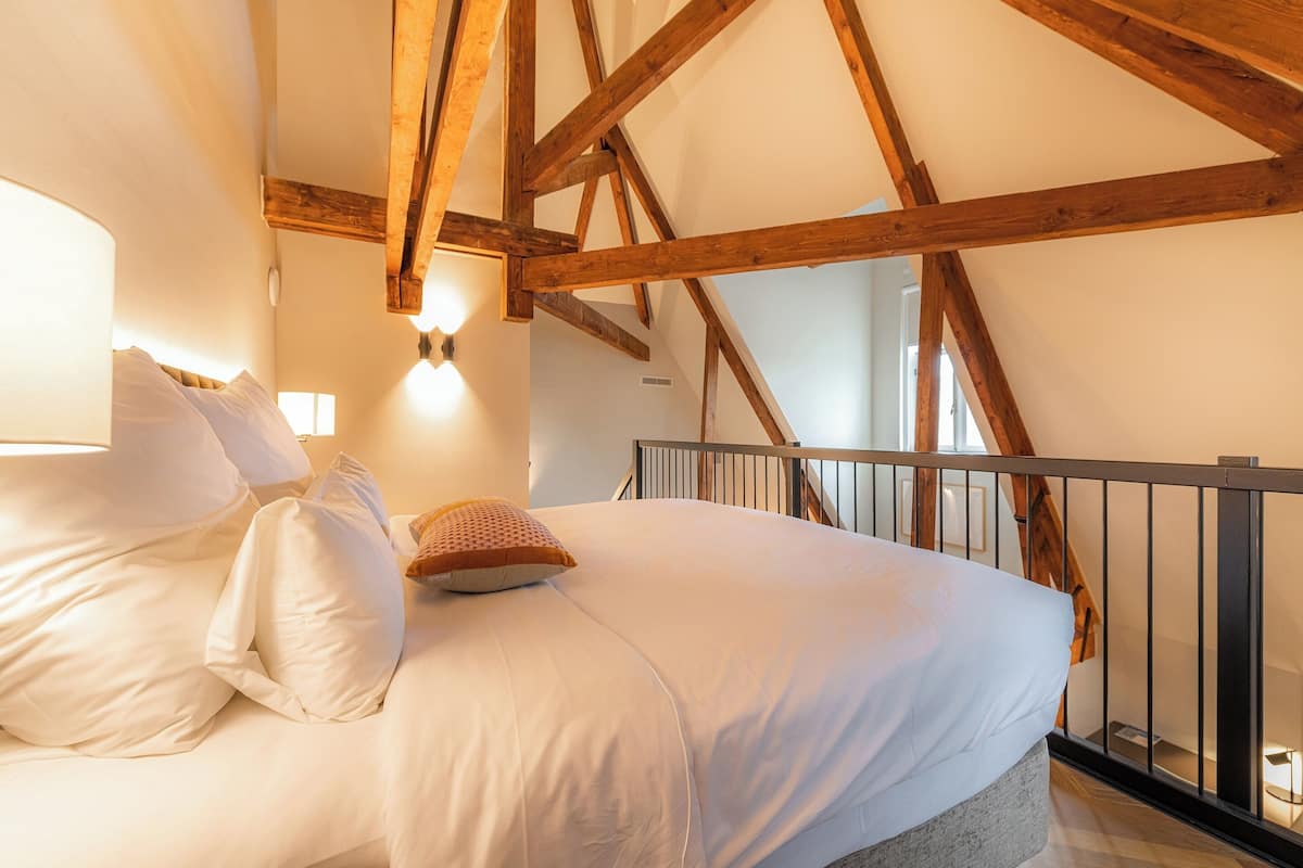 A bedroom with a large bed, wooden beams, a black railing, and a light fixture above the bed.