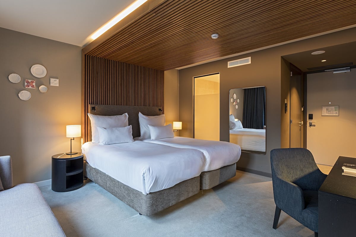 A modern hotel room with a large bed, bedside tables, a desk, and a mirror.