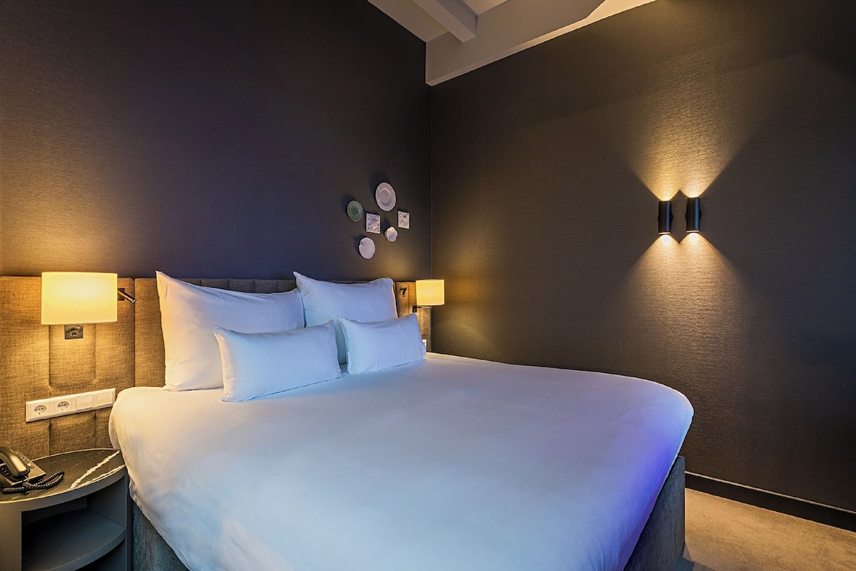 A hotel room with a large bed, two bedside lamps, a phone on a bedside table, and wall-mounted light fixtures.