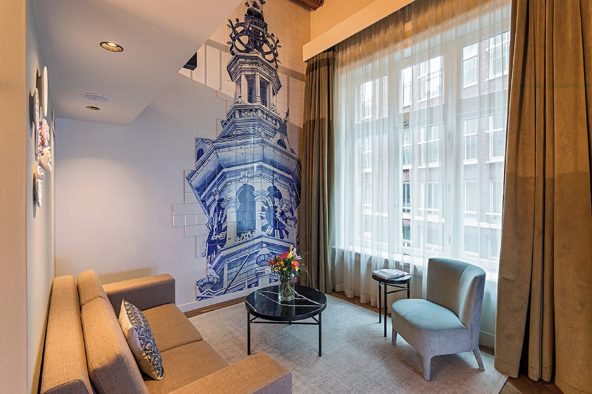 A living room with a sofa, armchair, coffee table, and a decorative wall mural.