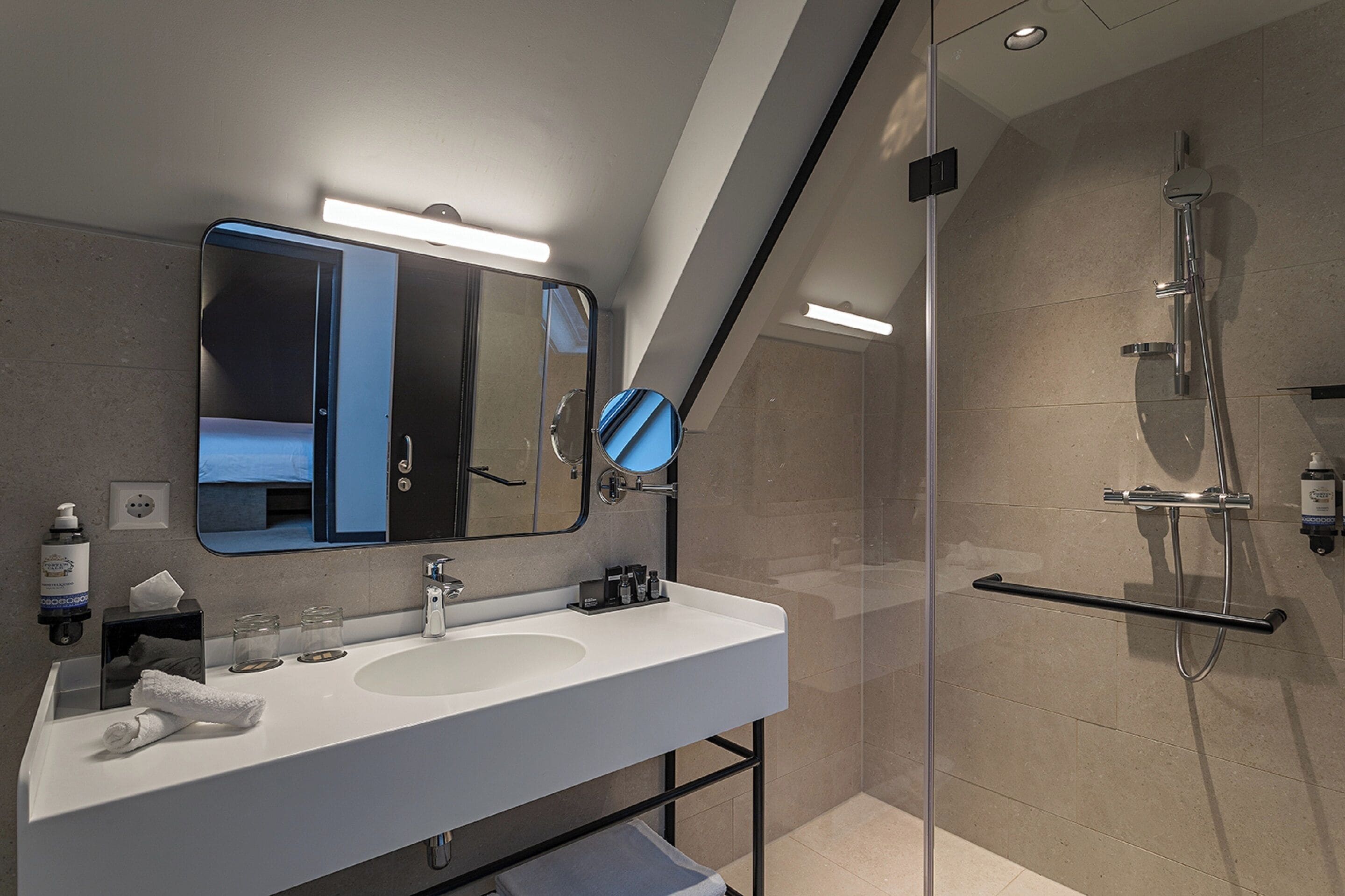 Un bagno moderno con uno specchio grande, un lavandino bianco e zona doccia con pareti in vetro.